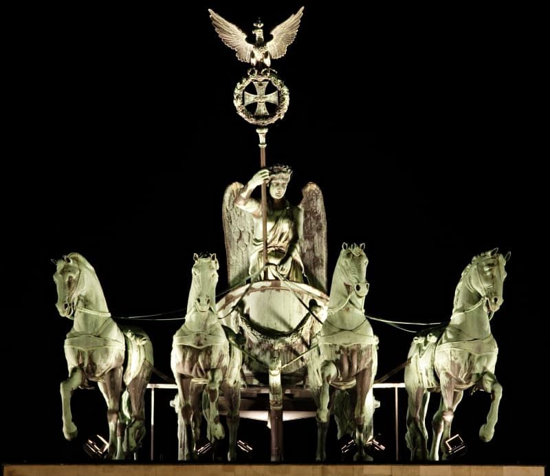 Fotografia della statua che sta sopra alla Porta di Brandeburgo di Berlino che rappresenta una dea alata con un'asta in mano e che guida un carro con 4 cavalli