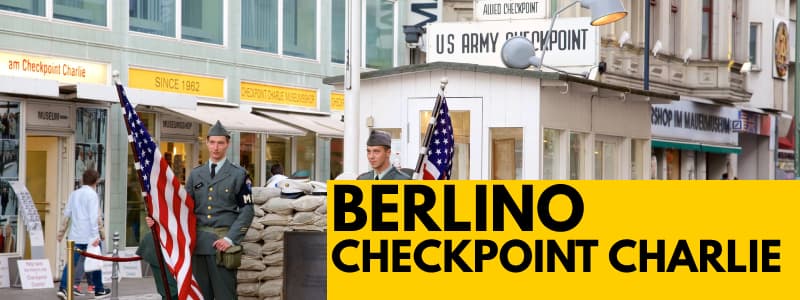 Fotografia del punto di controllo militare Checkpoint Charlie di Berlino con due soldati ed un rettangolo giallo in basso a destra con scritta nera "Berlino Checkpoint Charlie"