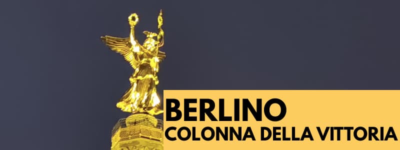 Fotografia della statua della Vittoria sulla cima della Colonna della Vittoria di Berlino di notte con rettangolo giallo in basso a destra con scritta "Berlino Colonna della Vittoria"