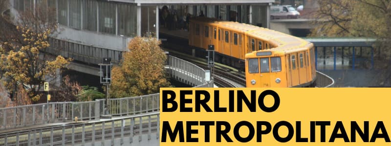 Fotografia della metropolitana di Berlino con treno giallo sulle rotaie all'aperto con rettangolo giallo in basso a destra con scritta nera "Berlino Metropolitana"