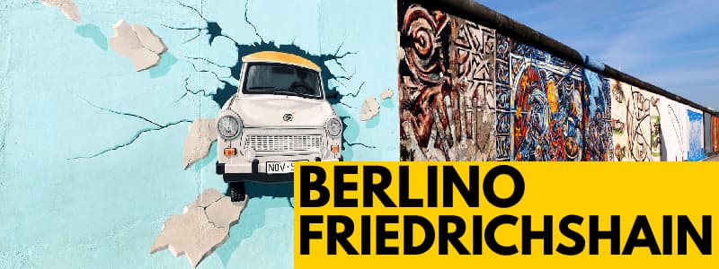Fotografia di un graffito di un'automobile che sfonda un muro azzurro ed altri graffiti sulla destra e rettangolo giallo in basso a destra con scritto "Berlino Friedrichshain"